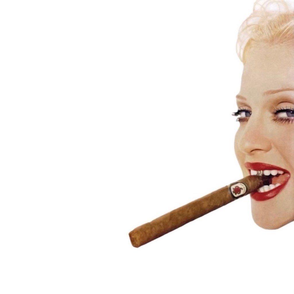 A woman with blonde hair and red lips smiles while holding a cigar in her mouth.