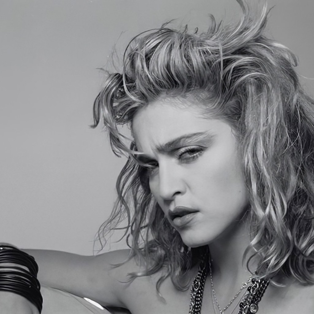 Black and white portrait of a woman with wavy hair, a serious expression, and wearing jewelry.
