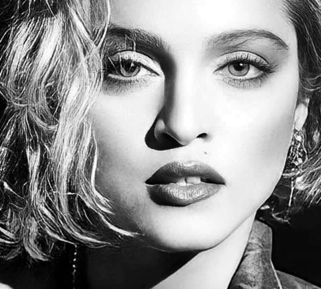 Close-up black and white portrait of a woman with short, wavy hair and striking facial features, highlighting her eyes and lips.