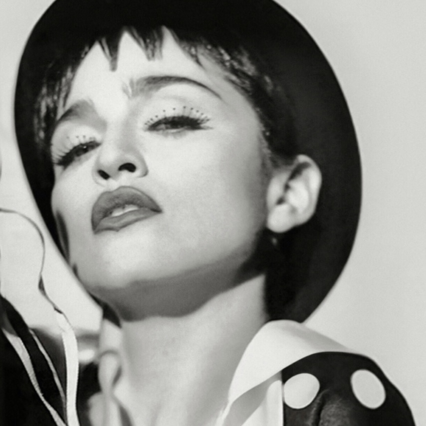 Black and white portrait of a woman with short hair wearing a wide-brimmed hat and a polka-dot outfit, posing confidently with a strong facial expression.