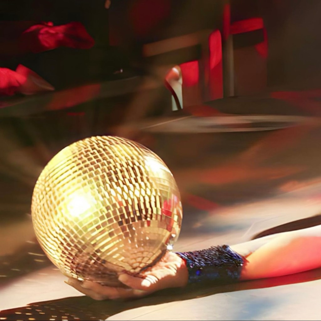 A hand holding a sparkling gold disco ball, with reflections and colorful lighting in the background.