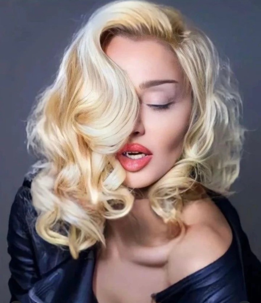 Close-up portrait of a woman with wavy blonde hair, partially covering her face, wearing bold red lipstick and a black leather top.