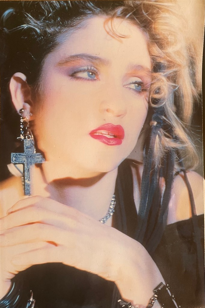 Close-up portrait of a woman with curly hair, wearing bold makeup and a cross earring, gazing thoughtfully.