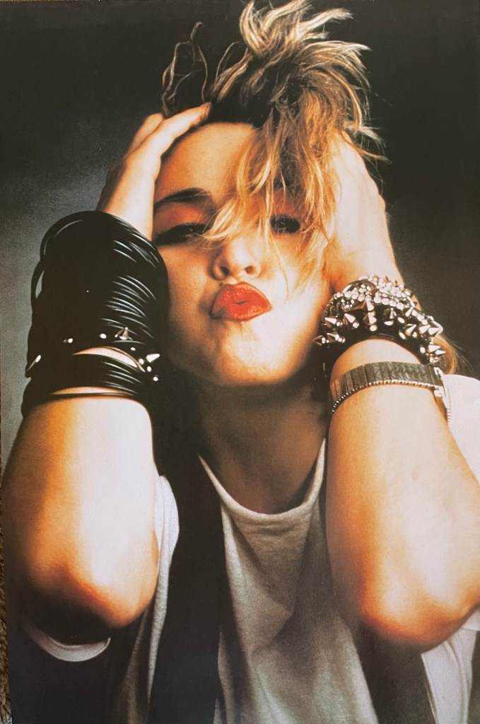 Close-up portrait of a woman with tousled hair, showcasing bold red lips and wearing leather bracelets, striking a playful pose with her hands on her head.