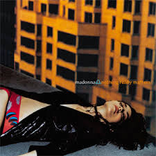 Album cover featuring a woman lying on the ground, dressed in a black jacket and colorful underwear, with a backdrop of a building and warm colors.