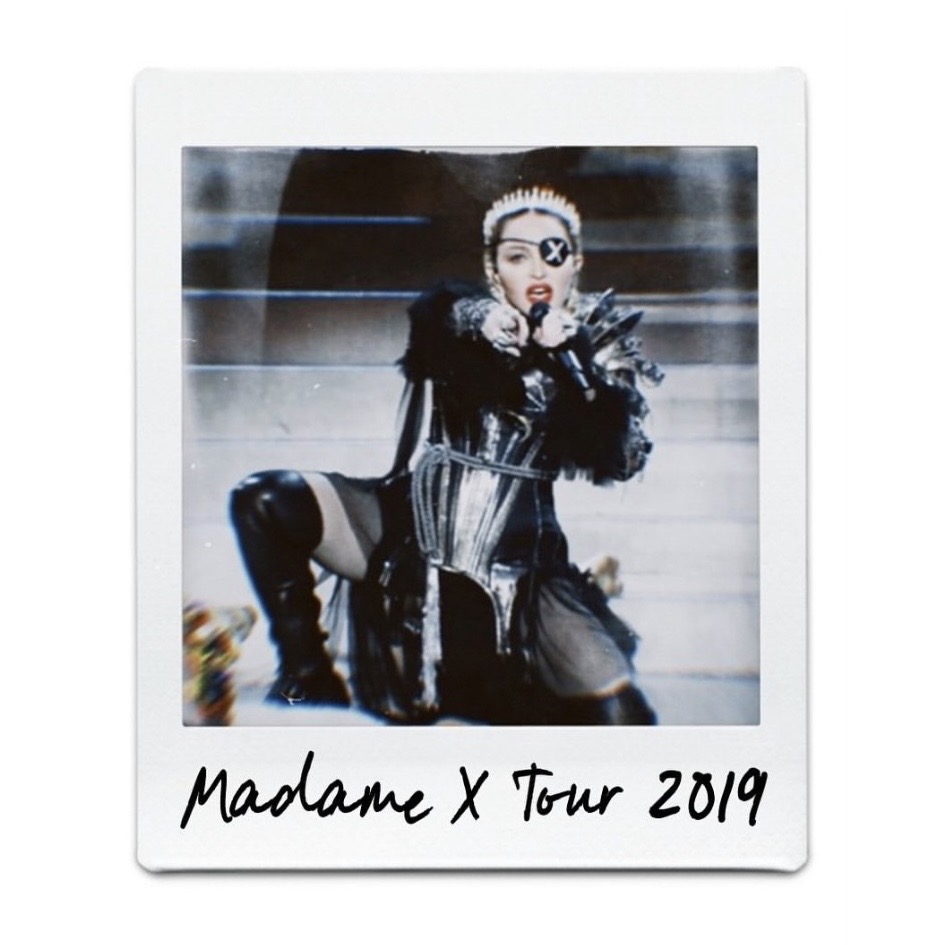 A performer in a dramatic costume with an eye patch, striking a dynamic pose on stage during the Madame X Tour in 2019.