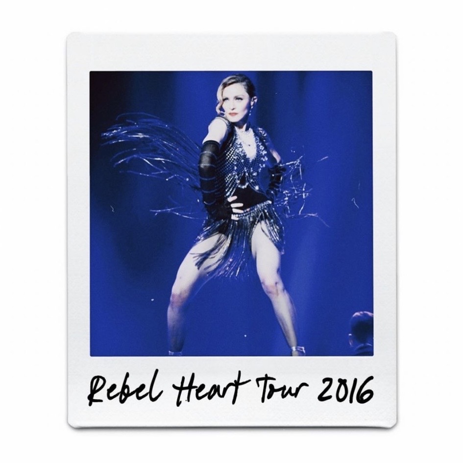 A performer wearing a sparkling outfit with feathered accents, striking a dynamic pose on stage during the Rebel Heart Tour 2016.
