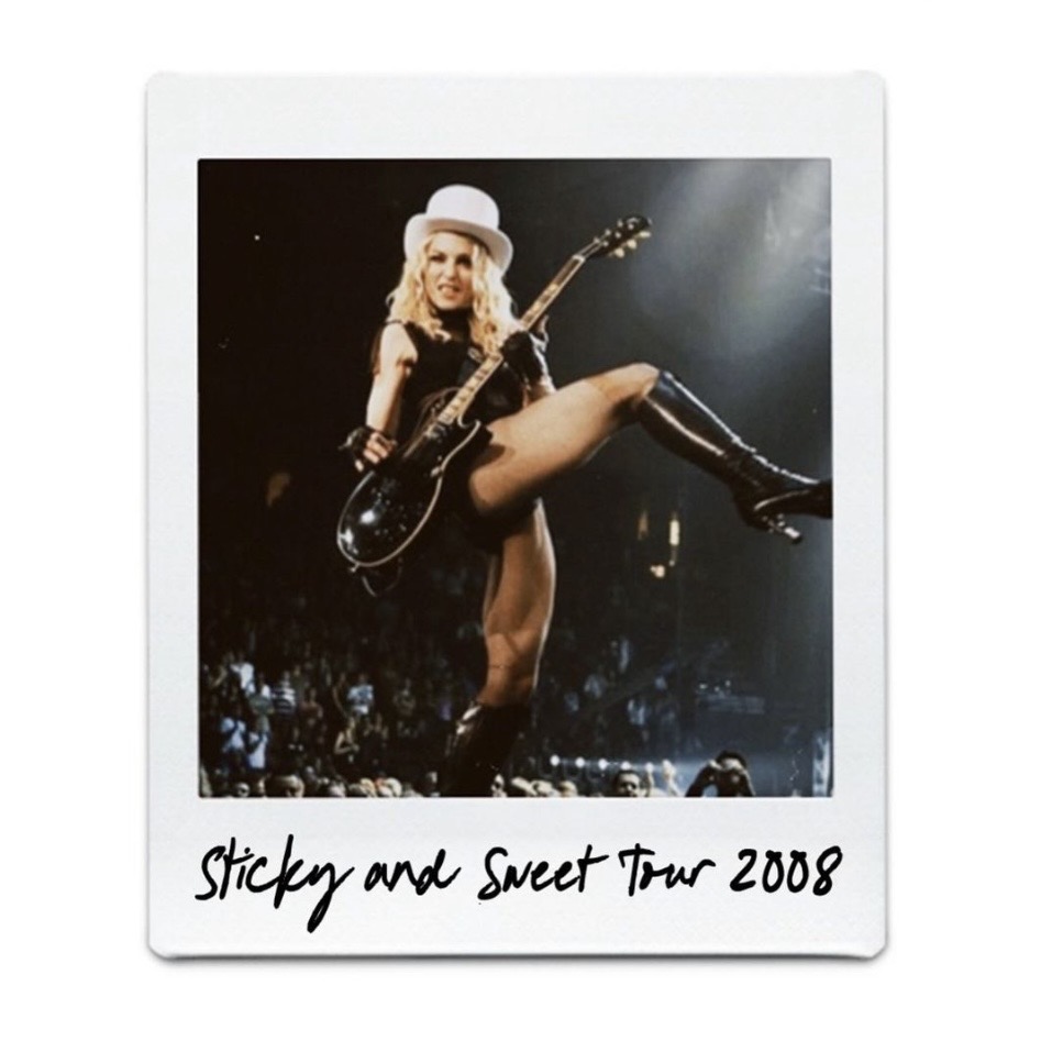 A female performer on stage during the Sticky and Sweet Tour in 2008, wearing a top hat, black outfit, and thigh-high boots, playing an electric guitar.