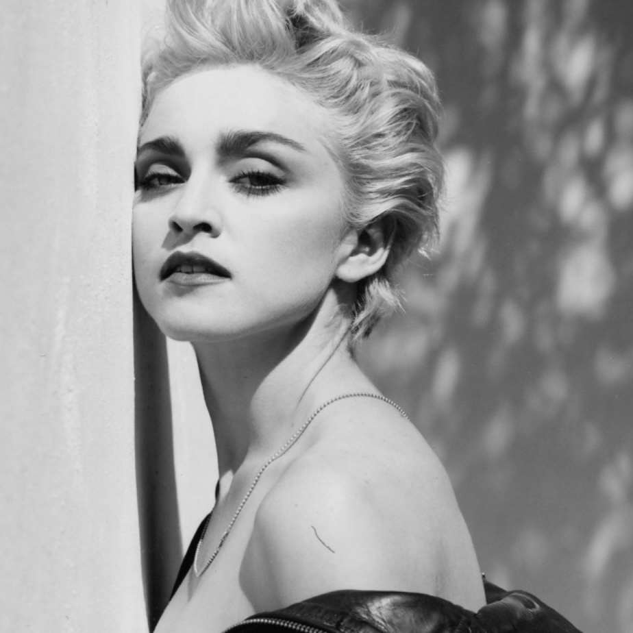 Close-up portrait of a woman with short, light blonde hair, gazing intently while leaning against a wall; captured in black and white.