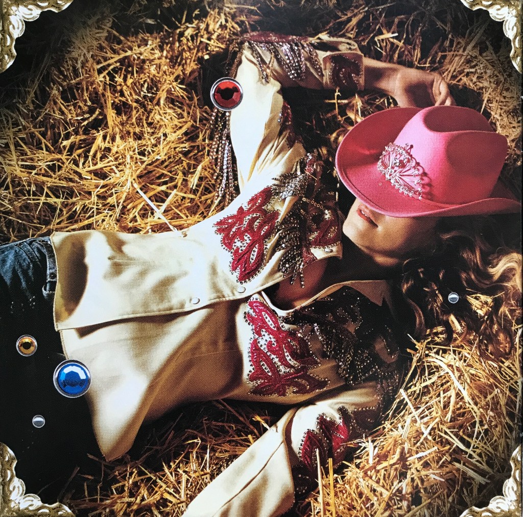 A woman lying on straw wearing a decorative western-style shirt and a pink cowboy hat.
