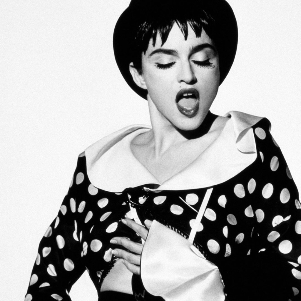 Black and white image of a woman wearing a polka dot outfit and a hat, singing passionately with her eyes closed.