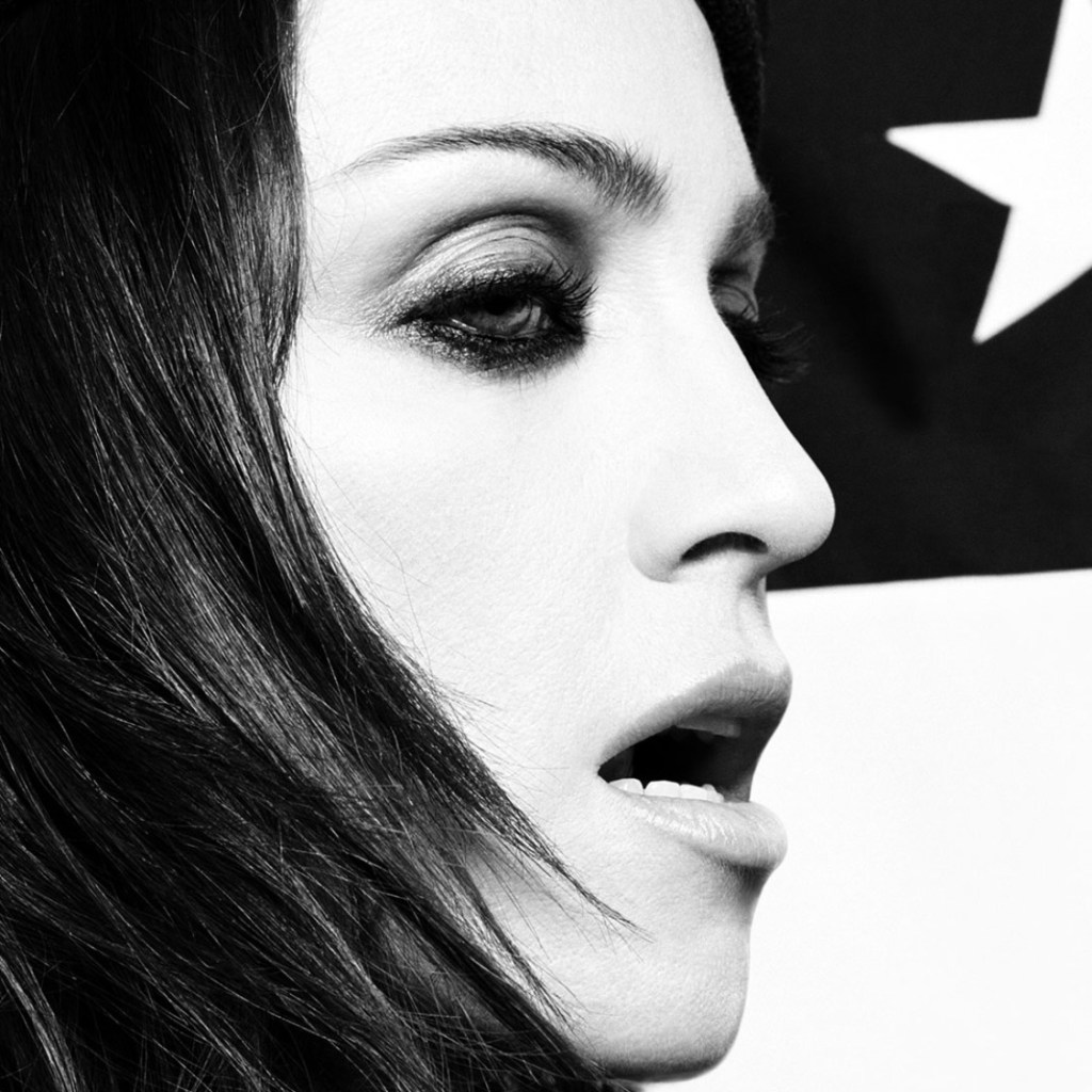 Black and white profile portrait of a woman with long hair, showcasing dramatic makeup and an opened mouth, with a star and striped background.