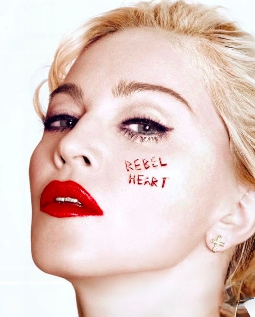 Close-up portrait of a woman with blonde hair, bold red lips, and the phrase 'REBEL HEART' written on her cheek, set against a light background.