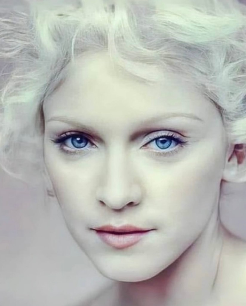 Close-up portrait of a woman with pale skin and curly white hair, featuring striking blue eyes and a neutral expression.