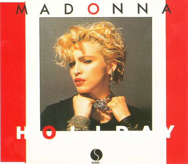 Cover art for Madonna's 'Holiday' single featuring the artist with short blonde hair, wearing bohemian jewelry, and a black outfit against a minimalist background.