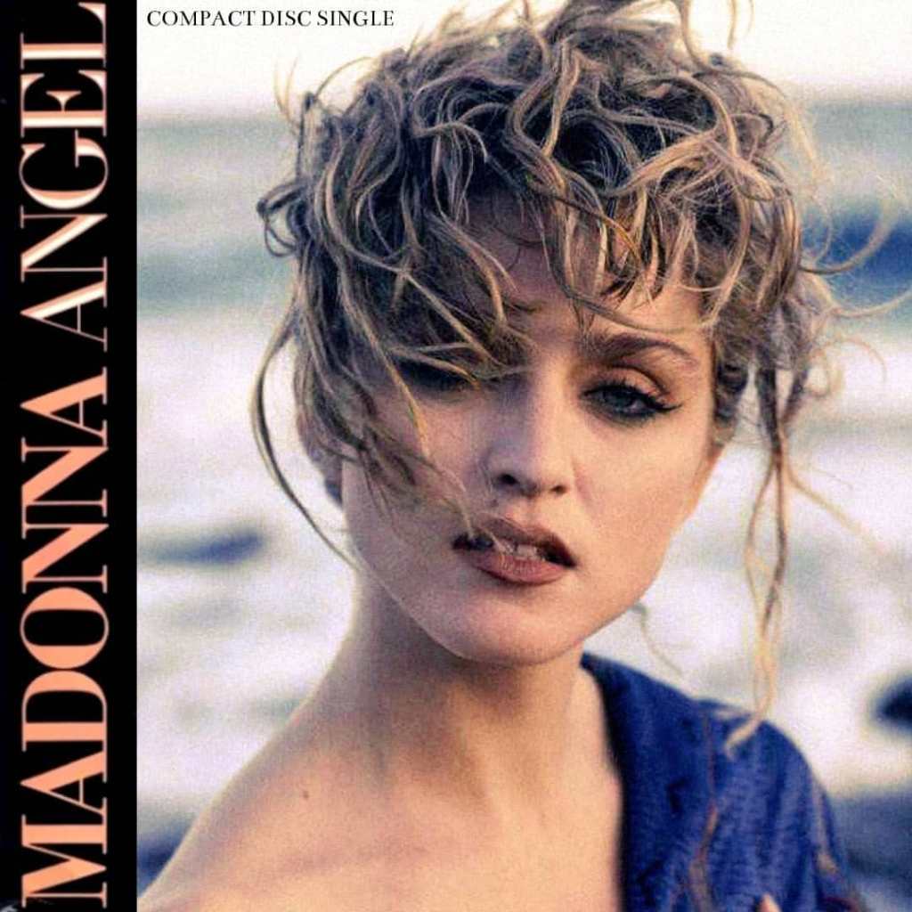 Close-up of a woman with curly hair, wearing a blue top, against a blurred background of ocean and sky, featuring the text 'Madonna Angel Compact Disc Single' on the left side.