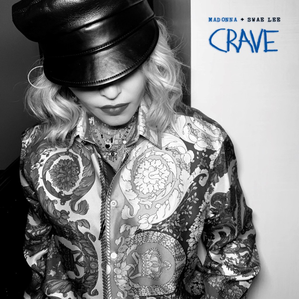 Artist Madonna in a stylish patterned shirt and leather hat, looking down. The image has a black and white filter with the text 'MADONNA + SWAE LEE CRAVE' in blue.