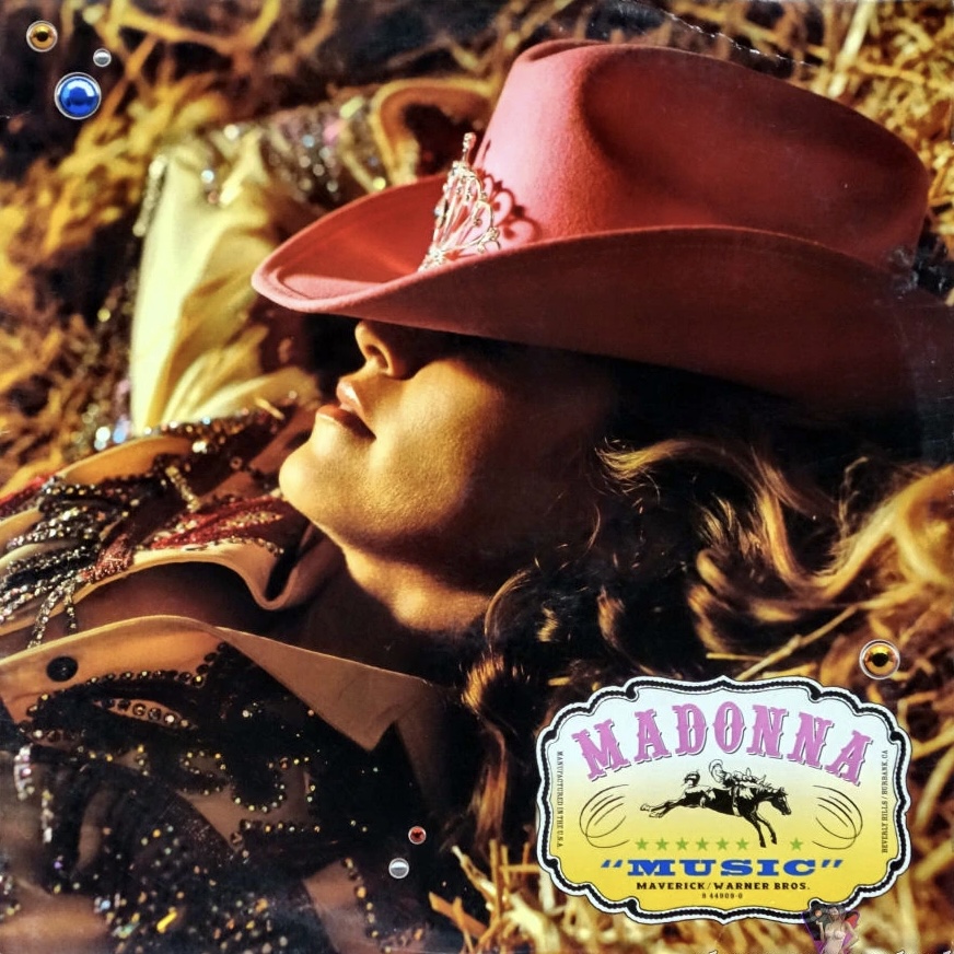 Close-up of a woman wearing a pink cowboy hat with embellishments, lying on a bed of straw, showcasing wavy hair and a subtle smile.