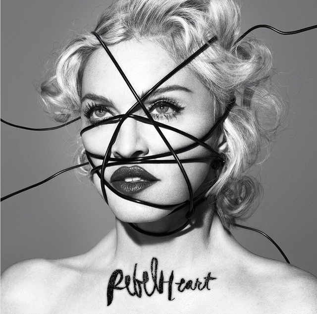 Portrait of a woman with short, wavy hair styled in curls, partially obscured by black wires. The image is in black and white, with the word 'rebellion' artistically integrated into the design across the chest.
