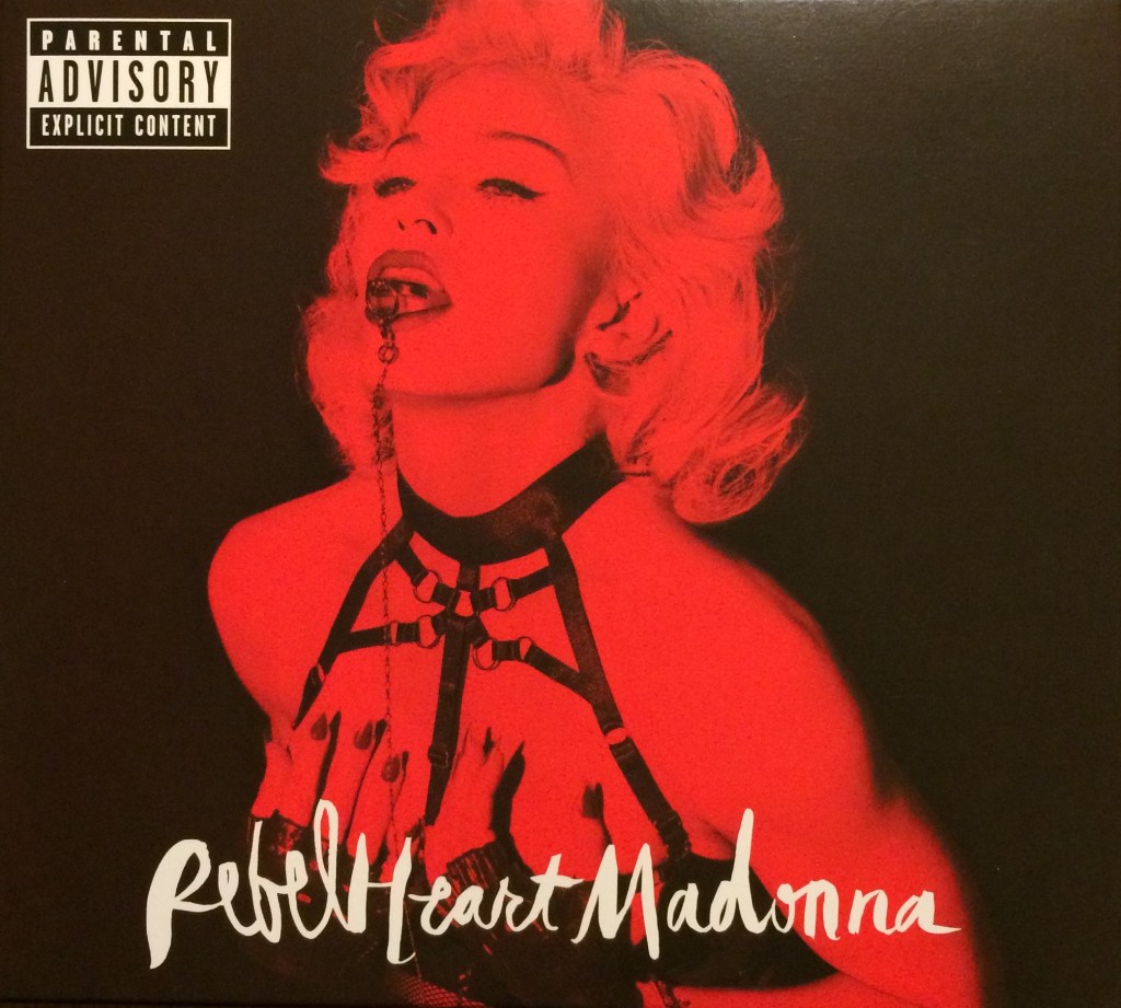 Album cover for 'Rebel Heart' by Madonna featuring a high-contrast red and black photo of a woman with blonde hair and bold makeup, wearing a black harness.