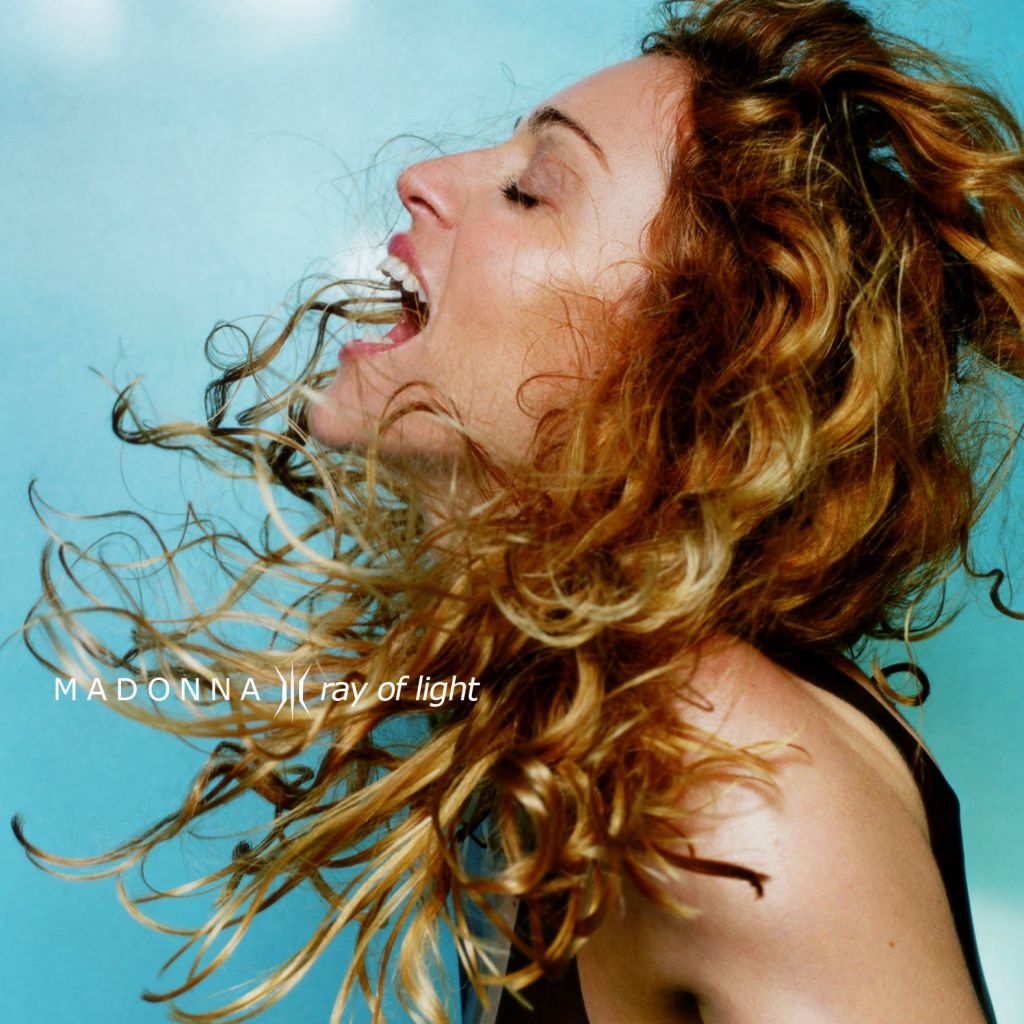 Profile view of a woman with curly hair, passionately singing or shouting against a blue background, with the text 'MADONNA ray of light' integrated into the image.