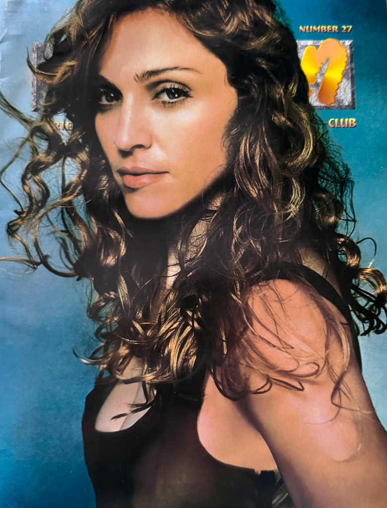 A portrait of a woman with long, wavy hair, gazing towards the camera with a subtle expression, against a blue background with text that appears to reference a club or magazine.