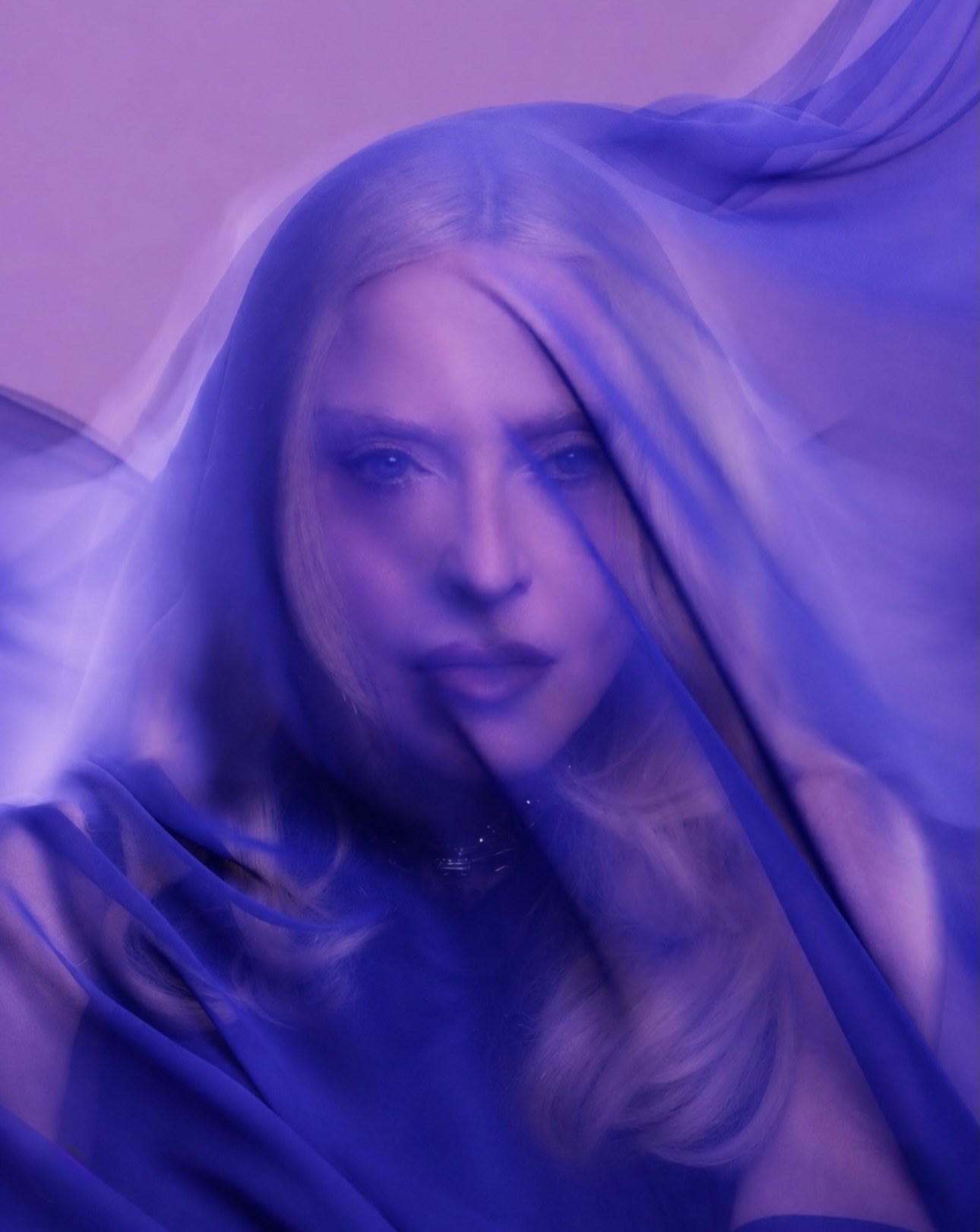 A close-up of a person partially obscured by flowing purple fabric, with soft, blended features and straight blonde hair.